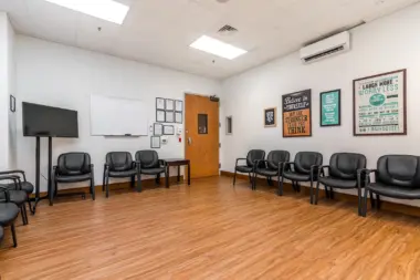 Interior meeting space with wooden flooring, black office chairs, whiteboard, inspirational wall signage, and television monitor.