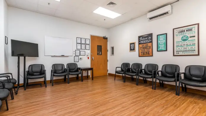 Interior meeting space with wooden flooring, black office chairs, whiteboard, inspirational wall signage, and television monitor.