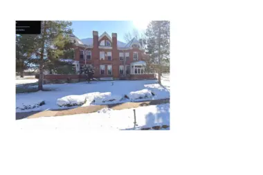 Exterior view of red brick Victorian-style building with snow-covered grounds and surrounding pine trees