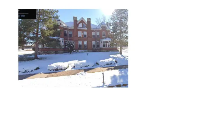 Exterior view of red brick Victorian-style building with snow-covered grounds and surrounding pine trees
