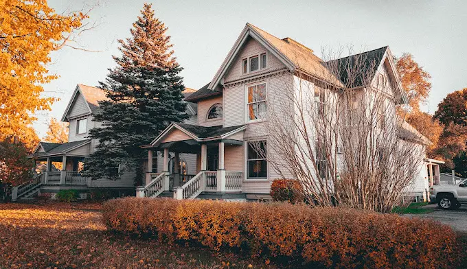 Exterior view of large Victorian-style residential building with multiple gables, surrounded by autumn trees and landscaping