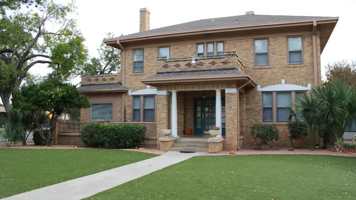 Exterior two-story brick residential building with white columns, covered front porch, landscaped lawn and mature trees
