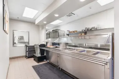 Interior commercial kitchen with stainless steel cooking equipment, prep stations, shelving, and polished floors