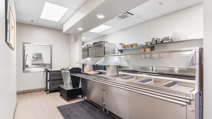 Interior commercial kitchen with stainless steel cooking equipment, prep stations, shelving, and polished floors