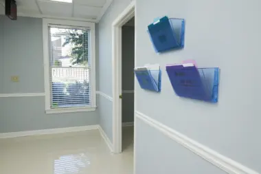 Interior hallway with light walls, window access, mounted document holders, entry doors with facility policies