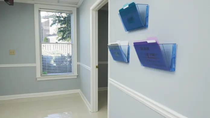 Interior hallway with light walls, window access, mounted document holders, entry doors with facility policies