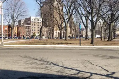 Outdoor view of Lincoln Park with mature trees, building facades, and paved grounds on clear day