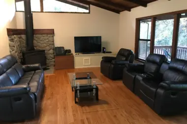 Interior living room featuring fireplace with stone surround, black leather recliners, television, and wood flooring
