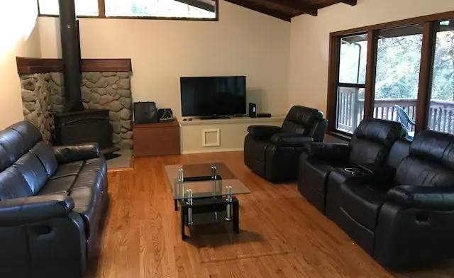 Interior living room featuring fireplace with stone surround, black leather recliners, television, and wood flooring