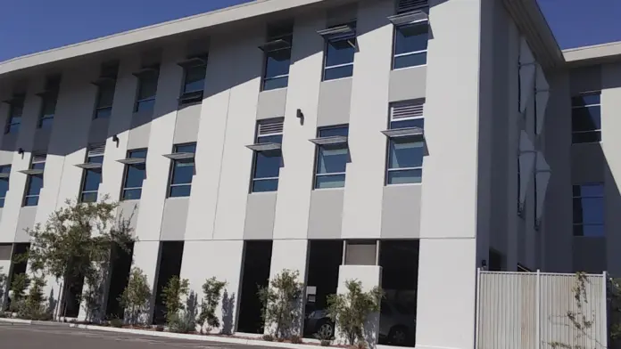 Exterior view of modern white multi-story treatment facility building with large windows and ground-level parking area