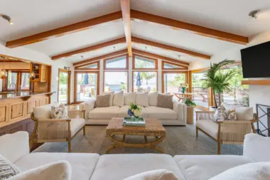 Interior common lounge featuring multiple seating areas, wooden beams, fireplace, and expansive windows overlooking ocean and landscaped grounds