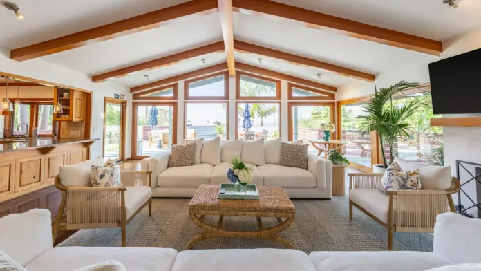 Interior common lounge featuring multiple seating areas, wooden beams, fireplace, and expansive windows overlooking ocean and landscaped grounds