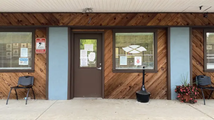 Exterior front entrance of wood-clad treatment facility with brown door, windows, concrete walkway, and potted flowers