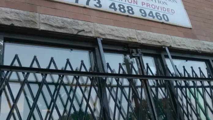 Exterior brick facade showing facility signage with service offerings and phone number, black security gate over windows and entrance.