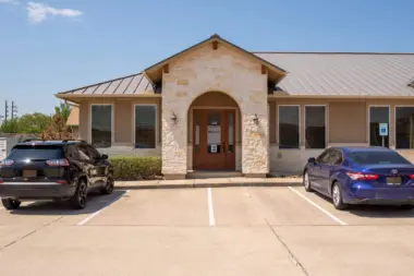 Exterior of treatment facility showing tan and stone building with arched entrance door, metal roof, and front parking area.