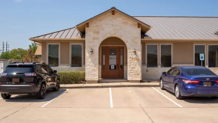 Exterior of treatment facility showing tan and stone building with arched entrance door, metal roof, and front parking area.