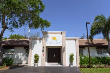 Exterior front entrance of treatment facility with A New Day logo, white facade, dark wooden doors, and landscaping