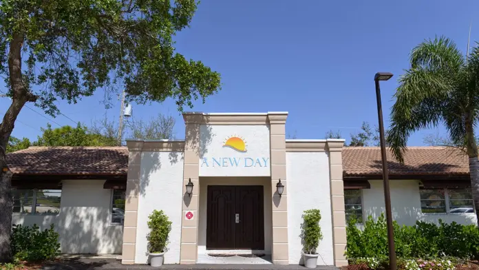 Exterior front entrance of treatment facility with A New Day logo, white facade, dark wooden doors, and landscaping