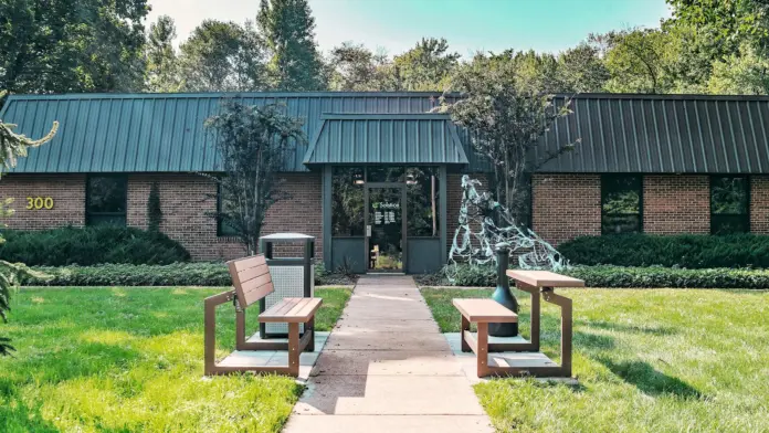 Exterior front entrance showing main doors under covered walkway with landscaping and sitting benches
