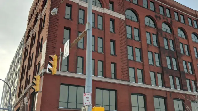 Exterior view of multi-story red brick building with regular windows, green awnings, and street-level entrance in urban setting.