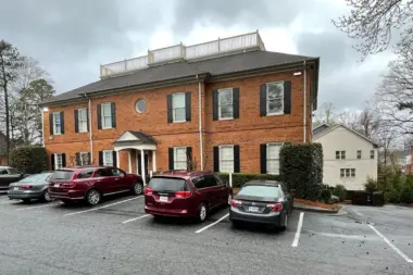 Exterior of brick treatment facility with columned entry portico, multiple parked vehicles, and landscaped grounds
