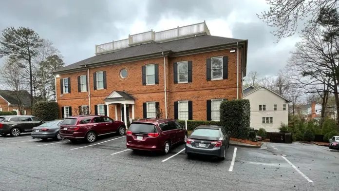 Exterior of brick treatment facility with columned entry portico, multiple parked vehicles, and landscaped grounds