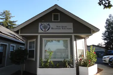 Exterior of main New Start Recovery Solutions entrance building with large front window, signage, white planters, and landscaping.