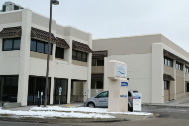 Exterior of modern treatment facility showing multi-story building facade, main entrance, windows, and front parking area in winter
