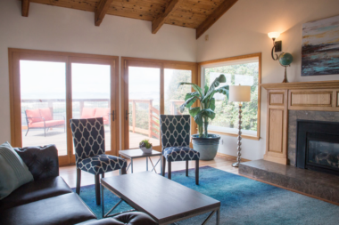 Interior lounge area with patterned accent chairs, fireplace, large windows, and views to outdoor patio