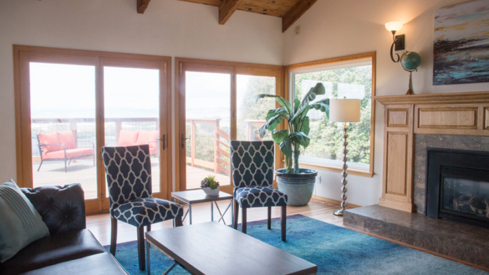 Interior lounge area with patterned accent chairs, fireplace, large windows, and views to outdoor patio