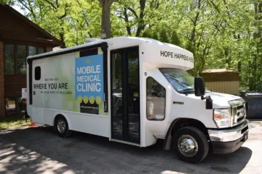 White mobile clinic van with blue and green text describing mobile medical services and recovery support