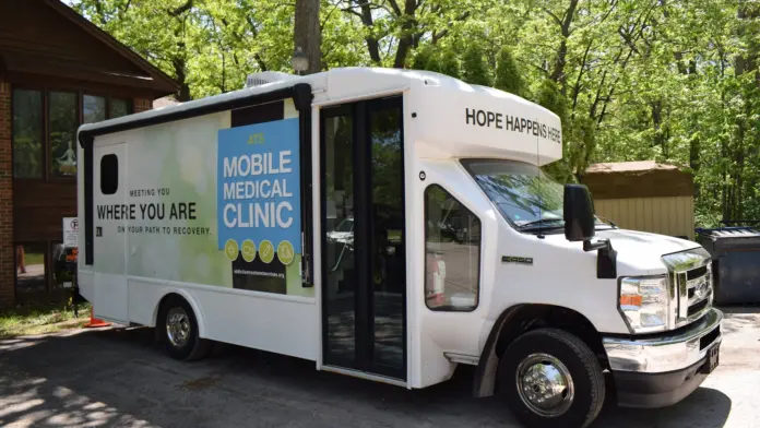 White mobile clinic van with blue and green text describing mobile medical services and recovery support