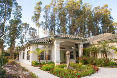 Exterior view of contemporary treatment center building with white facade, large windows, tile roof, and colorful garden landscaping