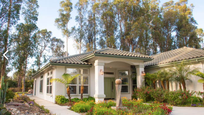 Exterior view of contemporary treatment center building with white facade, large windows, tile roof, and colorful garden landscaping