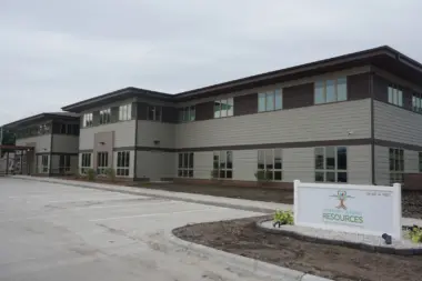 Exterior two-story residential building with gray siding, multiple windows, brick base, and facility signage