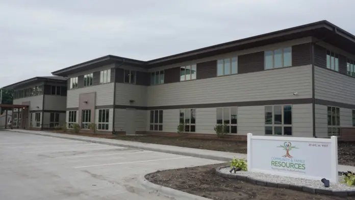 Exterior two-story residential building with gray siding, multiple windows, brick base, and facility signage