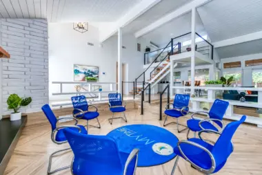 Interior group therapy room with multiple blue chairs arranged in circle, white walls, brick accent wall, and staircase