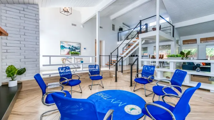 Interior group therapy room with multiple blue chairs arranged in circle, white walls, brick accent wall, and staircase