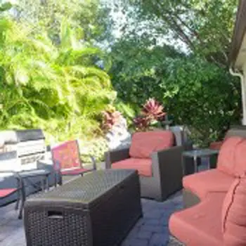 Outdoor patio with reddish lounge chairs, black side tables, lush green plants and trees overhead