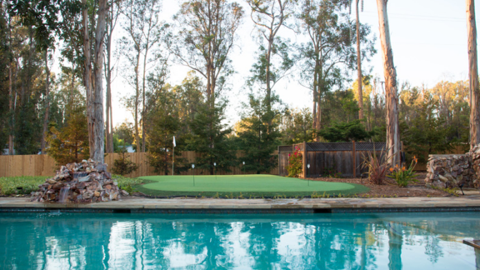 Exterior recreational area with swimming pool, putting green with flagstick, tall eucalyptus trees, and wooden lounge chairs