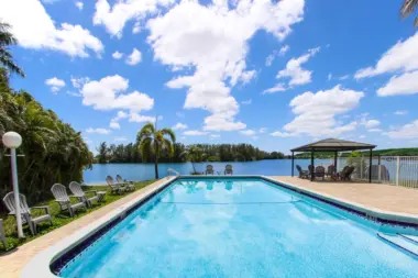 Outdoor resort-style swimming pool with lounge chairs, umbrellas, and waterfront views