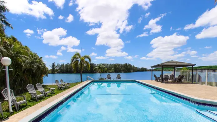 Outdoor resort-style swimming pool with lounge chairs, umbrellas, and waterfront views