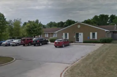 Exterior view of brick residential building with parking lot, vehicles, and landscaping