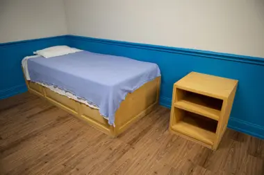 Interior bedroom showing single bed with blue linens, wooden nightstand, hardwood flooring, and blue accent wall