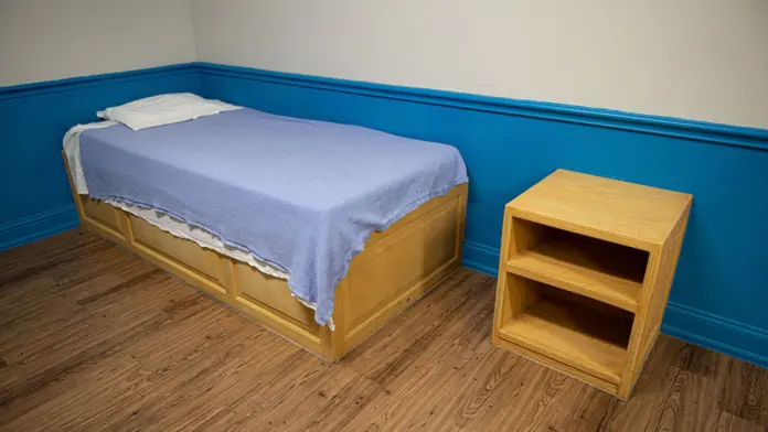 Interior bedroom showing single bed with blue linens, wooden nightstand, hardwood flooring, and blue accent wall