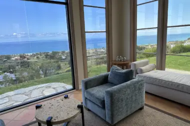Interior bedroom featuring bed, armchair, windows with distant ocean and coastal landscape views