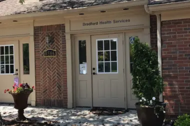 Exterior entrance showing cream-colored door frame, herringbone brick detailing, dormer windows, and planted flower arrangements.