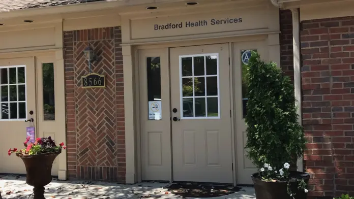 Exterior entrance showing cream-colored door frame, herringbone brick detailing, dormer windows, and planted flower arrangements.