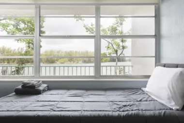 Interior patient bedroom with bed, white linens, and large windows overlooking waterfront landscape