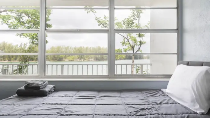 Interior patient bedroom with bed, white linens, and large windows overlooking waterfront landscape